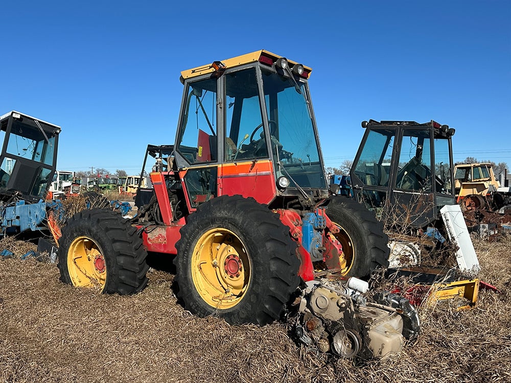 Dismembered red and yellow salvaged tractor with engine displayed behind it