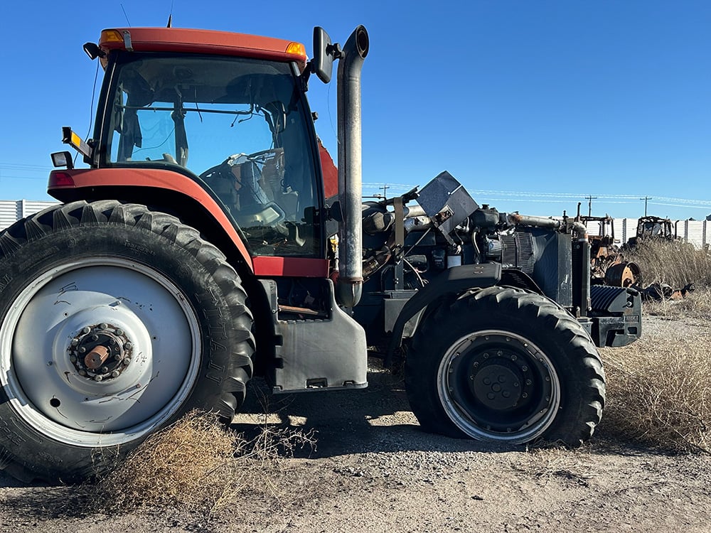Red salvaged tractor missing entire engine cover and broken wheel