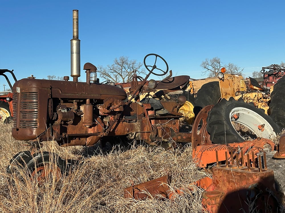Weathered tractor on display along with parts of a larger tractor next to it