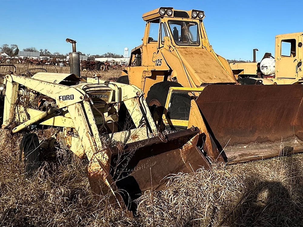 Yellow salvaged Ford Compact tractor next to larger equipment